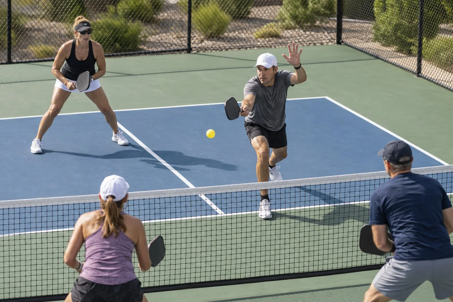 Pickleball doubles action showing one caller moving to a middle ball while the partner covers